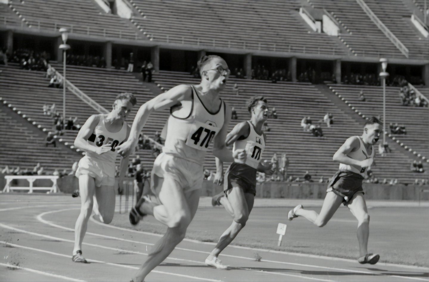 Cuatro atletas masculinos corriendo intensamente en una carrera de atletismo en un estadio.